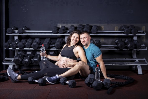 Pregnant woman goes for sports with her husband in gym for cross training. Couple athletes