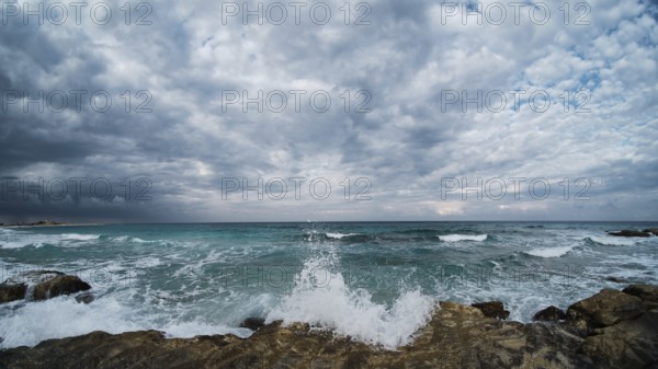 Waves of rushing sea are crashing over rocky coastline. Sea waves break upon rocks. Ultra-wide