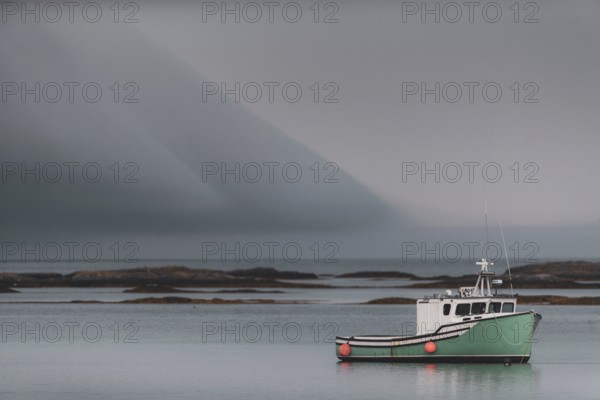 A commercial fishing boat sits tied to its mooring with dramatic clouds above, behind it are shoals