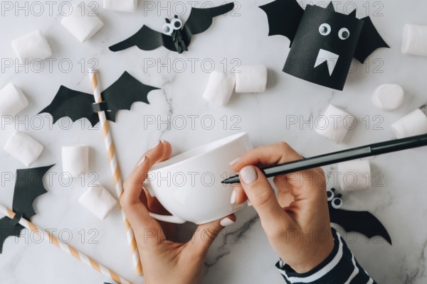 Female hands paint on white cup scary jacks face DIY for kids Halloween home activities Holiday art