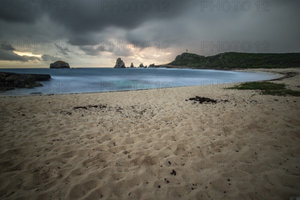 A secluded bay with a sandy beach in the morning. At the end of the beach a pointed rock formation