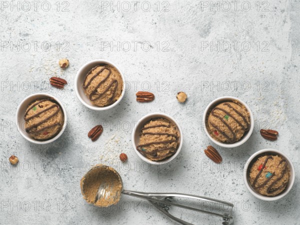 Safe-to-eat raw monster cookie dough in small portion bowl, ice cream scoop and nuts on gray cement