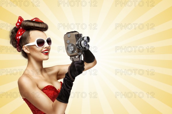 Glamorous pin up girl shooting a film with an old retro cinema 8mm camera on a colourful abstract