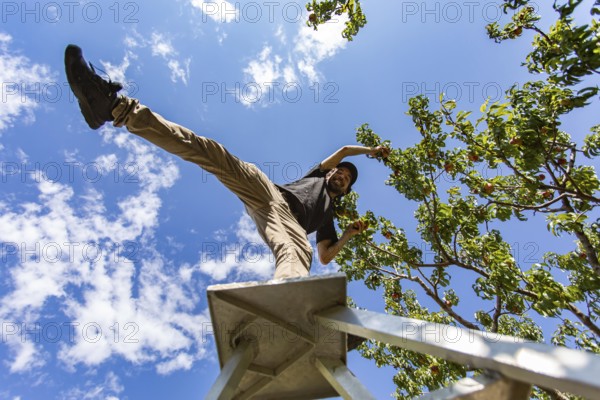 Low angle view of a caucasian man on the top of a ladder standing on one leg. as he enjoying