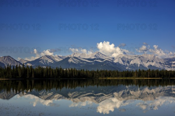 The Canadian Rockies and bright blue sky are reflected in a lake near Canmore, Alberta, Canada,