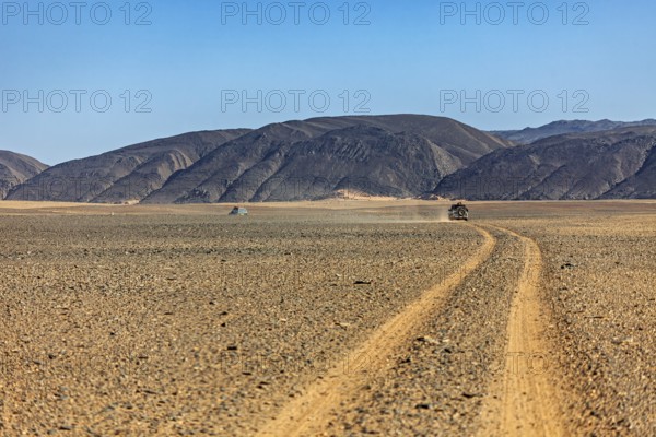 Dusty desert road leads through barren landscape with mountains, By off-road vehicle through the