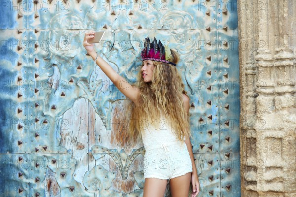 Blond teen girl tourist in Mediterranean old town door with colorful feathers on hair