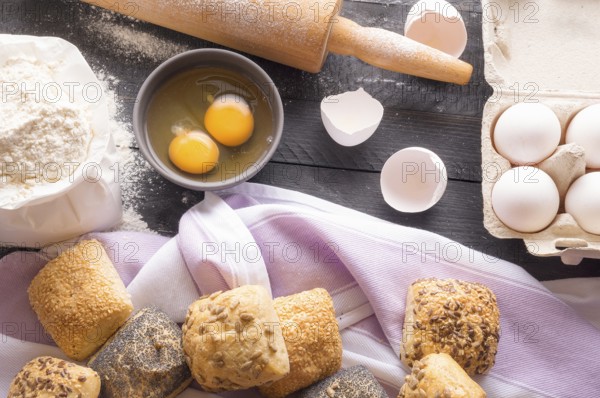 High angle view with a bag of flour, eggs, a rolling pin and freshly baked bread rolls, decorated