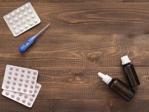 Medications or tablets and drops and electronic thermometer on a dark wooden background with copy