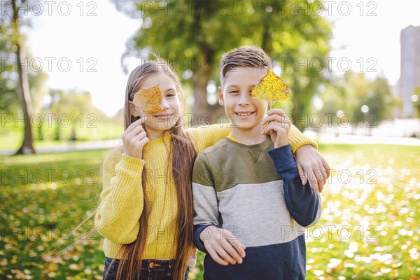 Happy Caucasian siblings enjoying in autumn day in park, sunny weather. Kids having fun holding