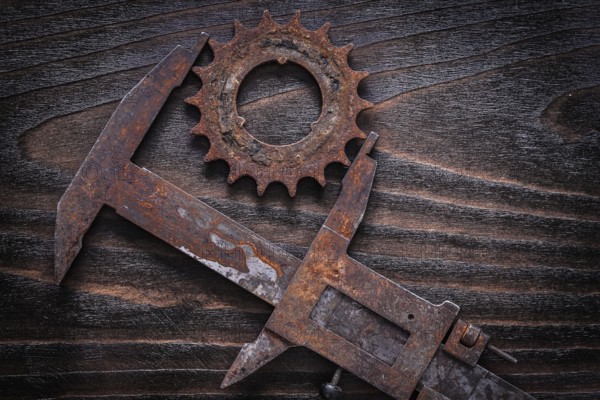 Rusted age-old measuring calipers with gear wheel on vintage dark wooden background construction