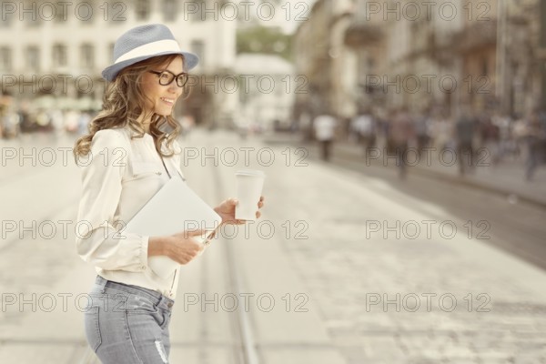 Beautiful young woman with a disposable coffee cup drinking coffee, holding a tablet in her hands