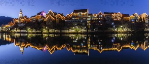 Christmas illuminated house facade of Frohnleiten reflected in the river Mur, panoramic shot, blue
