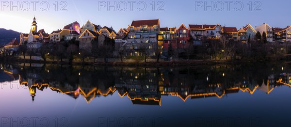 Christmas illuminated house facade of Frohnleiten reflected in the river Mur, panoramic shot, blue