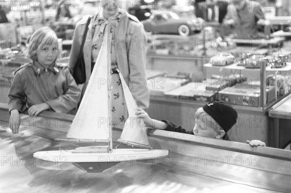 Toys in the 1950s. At a department store a boy is curious of the nice sailboat model floating in