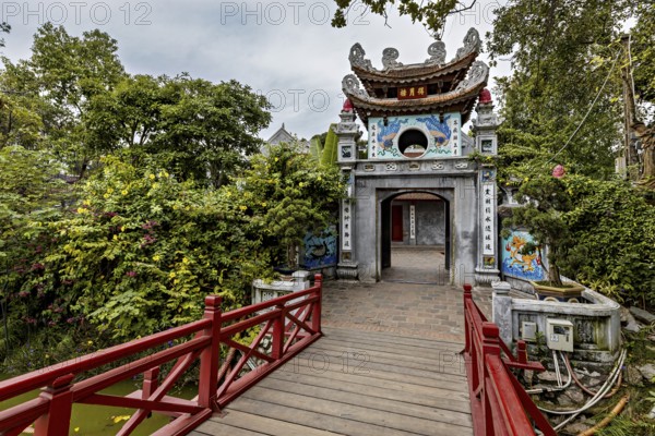 A richly decorated temple with a wooden walkway, surrounded by lush greenery and Asian