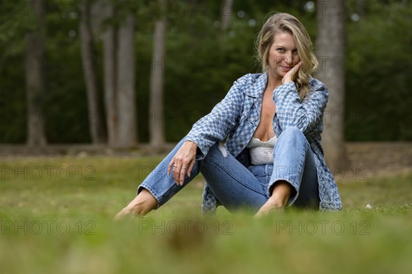 A beautiful blonde model enjoys the late summer sun outdoors. Surrounded by lush greenery and soft