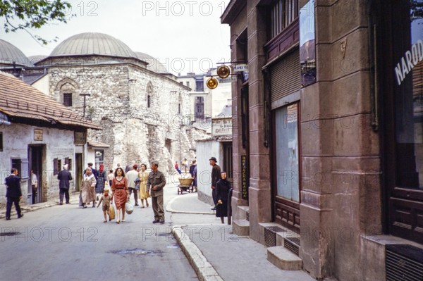 People walking along street of shops, next to domes of Brusa Bezistan museum, Sarajevo, Bosnia and
