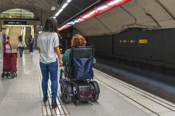 Rear view of a disabled caucasian adult woman in wheelchair and asian friend walking along metro
