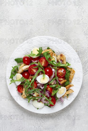 A warm salad with fried chicken fillet, arugula and cherry tomatoes, and boiled quail eggs, on a