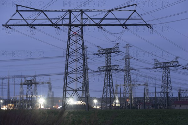 High-voltage pylons illuminated at dusk, industrial environment, quiet atmosphere, Wolmirstedt,