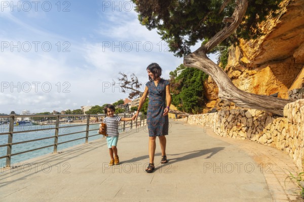 Mother and son enjoying a leisurely stroll along the scenic seaside promenade of puerto cristo,
