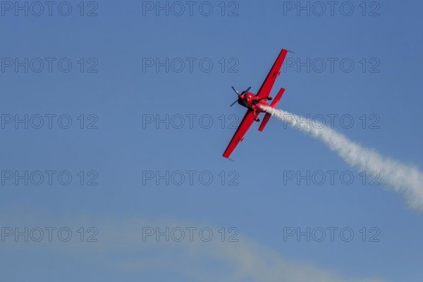 Red stunt aerobatic plane performing stunts in blue sky. Concept of speed, difficulty, precision,