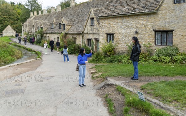 Tourists visiting famous Cotswold buildings at Arlington Row, Bibury, Gloucestershire, England, UK