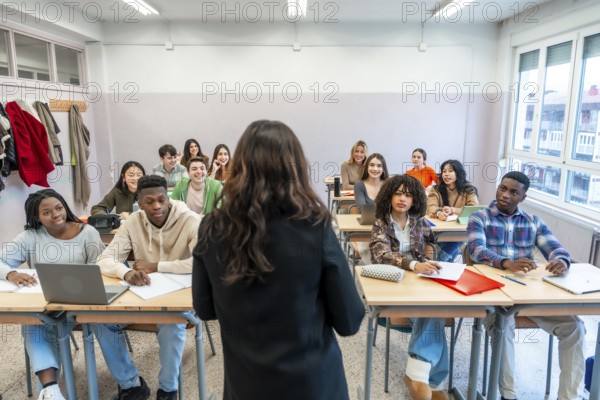 Female professor teaching a lesson to a multi ethnic group of students sitting at desks in a
