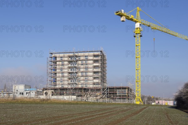 Unfinished building with yellow construction crane, construction site under blue sky, housing