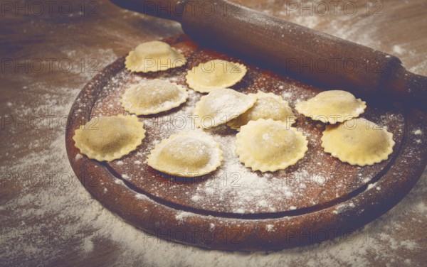 Fresh raw, uncooked ravioli, on a cutting board, with a rolling pin for dough, wooden background,