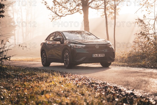 A Volkswagen on a country road in the morning sun mist between autumnal trees, electric car VW ID5,
