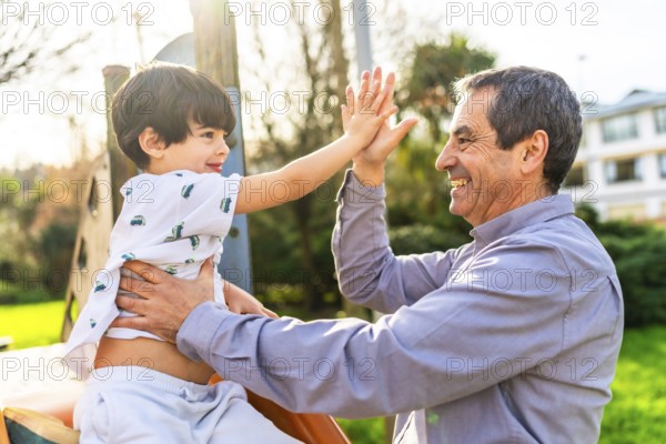 Grandfather and grandson are enjoying time together at the playground, giving a high five and