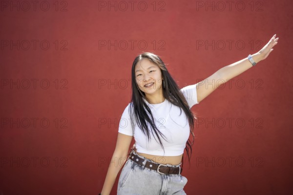 Frontal portrait of a happy beauty young asian woman raising arm dancing K-pop against a red urban
