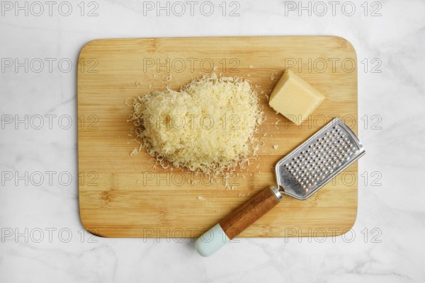 Shredded cheese on a wooden cutting board alongside a block of cheese and a grater. The items are