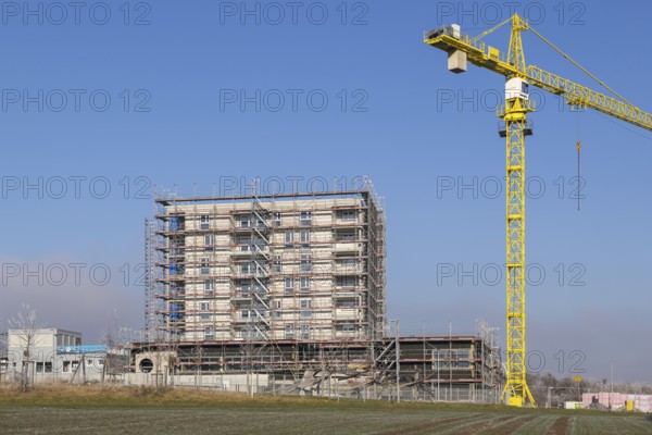 Incomplete building with yellow construction crane in clear sky, housing construction, new