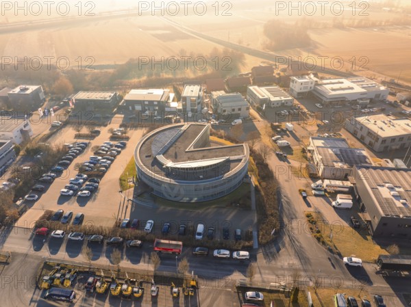 Round building in an industrial area with parked cars and street in the background in sunny