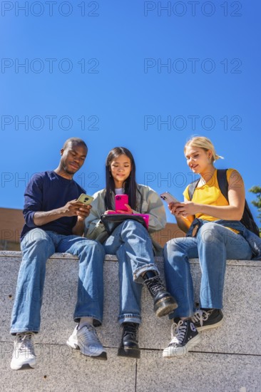 Vertical low angle view photo with copy space against blue sky of multi-ethnic students sitting on