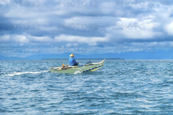 Traditional outrigger boat sailing on turquoise water with a fisherman wearing a straw hat, near