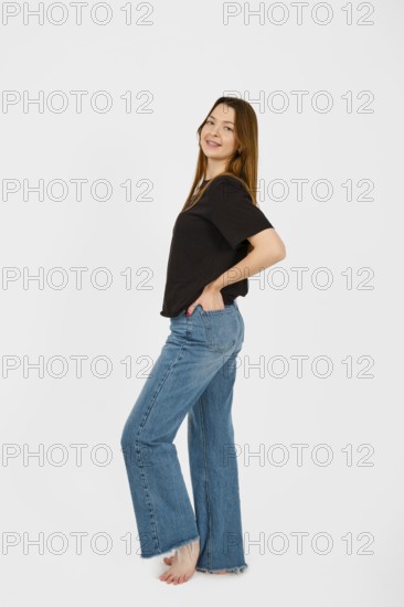 Barefoot woman stands with a playful posture, smiling at the camera while wearing a black top and
