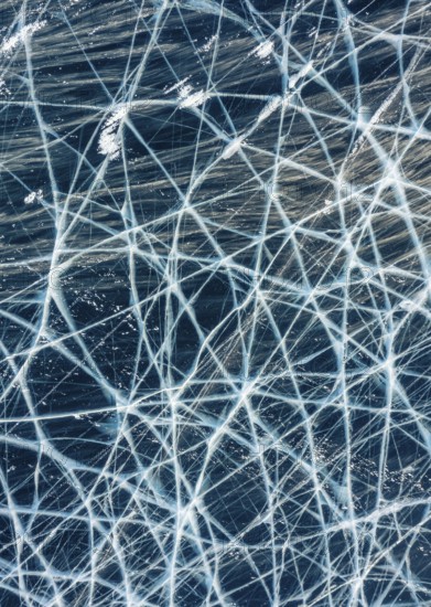 Aerial top view of frozen Lake Baikal. Blue transparent clear smooth ice with deep cracks. Wind