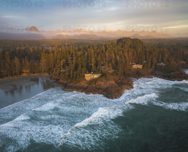 Aerial view of ocean waves crashing against a forested coastal island at sunset, with warm light