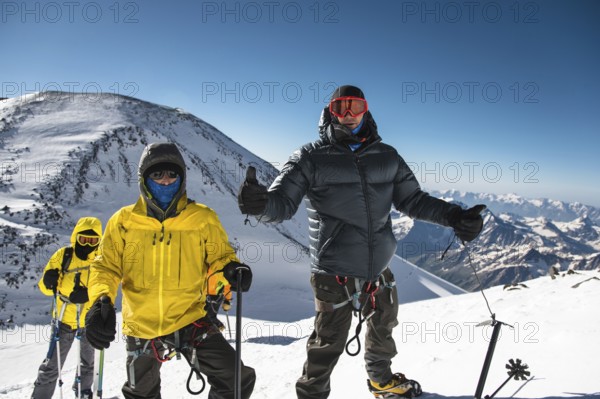 A middle-aged climber in a down jacket and harness shows a thumb up next to his friends on the way