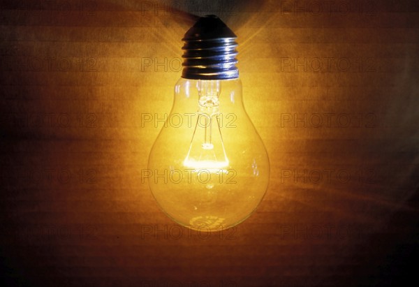 Closeup of an old burning light bulb, switched on, a carton as background is illuminated, lit with