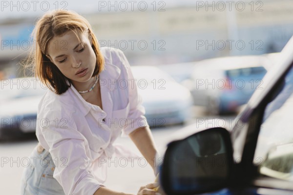 Woman concentrating while cleaning a car window with a sponge under sunlight
