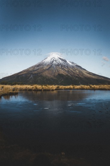 A snow-capped mountain reflected in a still lake under a clear blue sky, Mount Taranaki, New
