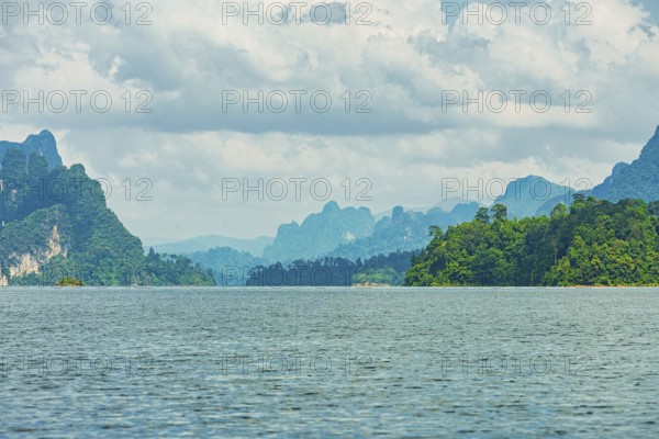 Distant mountains on a cloudy horizon overlook a vast lake, offering a calm natural scene, Cheow