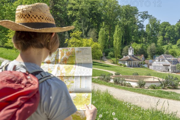 Woman with brown hair, gray t-shirt, jeans, red backpack and straw hat taking a break from her