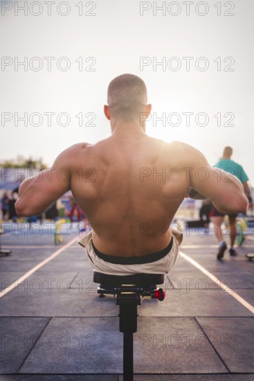 A man exercises outdoors in the sunlight, concentrating on strengthening his back muscles on a