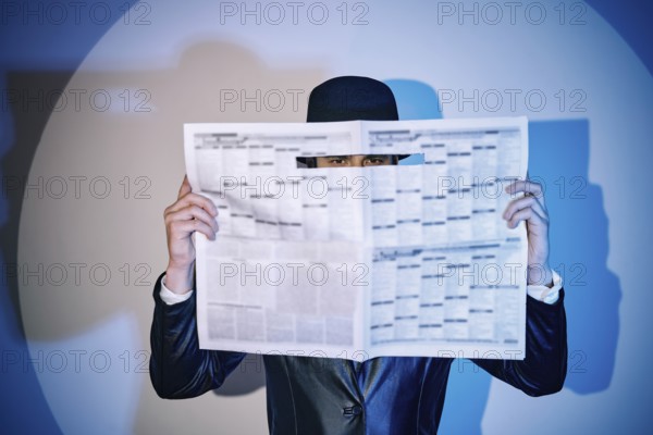 Man hiding watches through the newspaper in the spotlight on studio background. noir film style.